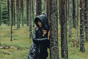 穿着黑色雨衣的女孩走在松林里