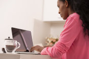 一个穿着粉色睡衣的女人在电脑上打字，早上喝着咖啡。