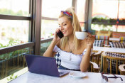 快乐的年轻时髦的女人喝着咖啡在咖啡馆里打电话。桌上的笔记本电脑