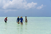 美丽，年轻，中年和老年妇女走在浅水在沙洲岛海滩四月，马尔代夫