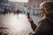 一个年轻女子在城里用智能手机发短信。