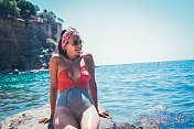 年轻性感的女人穿着泳衣站在岩石附近的水里