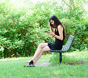 年轻的俄罗斯女子坐在长椅上，在公园的户外，使用手机