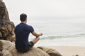 一名男子坐在岩石上在Pedn Vounder海滩放松