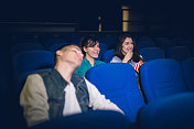三个朋友在电影院看电影，其中一个在睡觉。