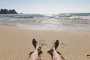 在Pedn Vounder海滩，康沃尔一个田园诗般的阳光明媚的一天，POV男人的腿日光浴。