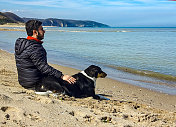 一个年轻人和他的狗坐在沙滩上看海平线