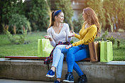 两个女人购物后坐在城市公园聊天