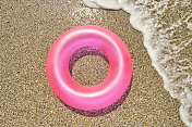 头顶上的一个粉红色的橡胶环在沙子上作为一个阳光明媚的夏天海浪打破它。