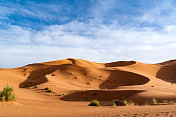 巨大的橙色沙状沙丘和多云的天空在Merzouga沙漠，摩洛哥。