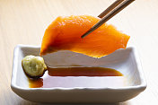 日本的生鱼片。用筷子夹起三文鱼片，加入酱油。