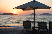 日落时分的热带海滩，配有沙滩椅和雨伞