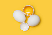 高角度的小组白色生鸡蛋，一个是破在黄色的背景
