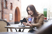 在咖啡馆外拿着冰沙和智能手机的女人