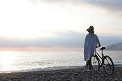 成熟的女人骑着自行车在日出的海滩上放松