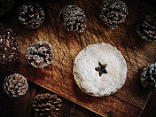 肉馅馅饼对着深色的木材表面，周围是覆盖着雪的节日松果。