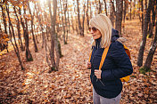 成熟的女性背着双肩包走在秋天的森林里