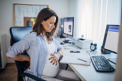 怀孕的女商人在办公室背痛。