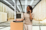 非裔美国女性站在仓库穿着纽扣衬衫，拿着清单和使用手机