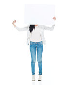 拉丁美洲和西班牙裔的年轻女性穿着牛仔裤，举着牌子站在白色背景前