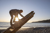 日出时，男子爬上海滩上的木柱