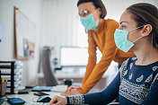 两名女性戴着防护口罩在办公室工作，以保护自己免受冠状病毒感染