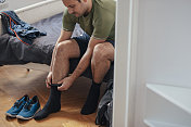 在家锻炼准备:一个帅气的男人坐在床上，穿上袜子和运动鞋去跑步