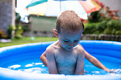 一个金发小男孩坐在一个嬉水池里