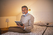 大胡子老人坐在床上使用他的数字平板电脑