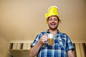 一个男人戴着派对饰品，拿着一大杯啤酒做鬼脸
