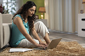 这是一个年轻女子坐在家里的地板上使用笔记本电脑和文书工作的照片，库存照片