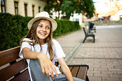 美丽的少女戴着太阳帽坐在城市公园的长椅上