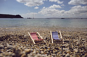 6月的一个阳光明媚的日子，康沃尔圣莫斯卵石海滩的海岸线上，两把迷你躺椅。