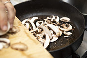 手把切好的蘑菇从木砧板上推到黑色的煎锅里