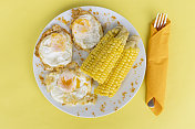眼睛上有黄色玉米的鸡蛋，盘子里有黄色背景。