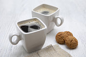 白色木桌上放着两个浓缩咖啡杯，还有杏仁饼干和餐巾