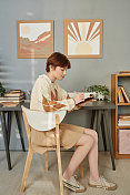 一头红短发的时尚女学生坐在舒适的房间里，在画板上做笔记