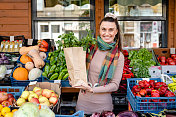 一个快乐的女人在市场上拿着一纸袋杂货的画像