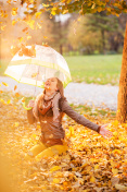 快乐的女孩坐在秋叶中，撑着伞。
