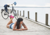 女人骑着自行车躺在湖边的码头上放松