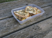 松露橄榄油涂在烤面包上，堆放在一个塑料容器里，放在木制的野餐桌上