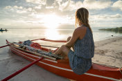 年轻女子坐在渔船上凝视夕阳，热带气候