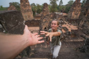 年轻女子攀登柬埔寨古庙，男子伸出援助之手登顶