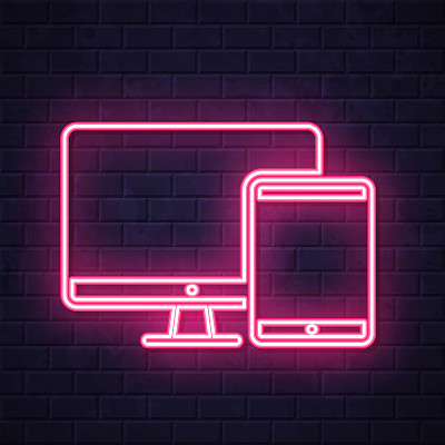 台式电脑和平板电脑。在砖墙背景上发光的霓虹灯图标
