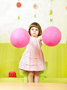 漂亮的小女孩在玩两个粉红色的气球