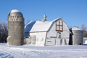 倾斜的白色谷仓旁边的筒仓在雪地上
