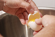 双手将鸡蛋打入不锈钢搅拌碗中。