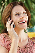 快乐成熟的女人拿着果汁杯在打电话