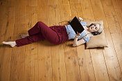年轻女子躺在地板上玩平板电脑。