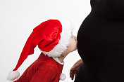 年轻女孩戴着圣诞帽，亲吻妈妈怀孕的肚子